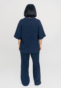 Marineblauw tweedelig set bestaande uit een kortemouw, gekraagde top en wijde broek, beide met een subtiele gestreepte textuur.