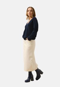 Granatowy sweter z dzianiny z dekoltem w serek, kremowa spódnica midi i granatowe botki na obcasie; cechuje go luźny krój, teksturowana tkanina oraz boczne kieszenie.