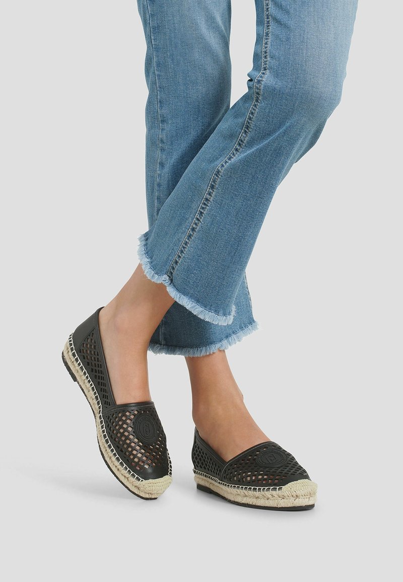 Chaussures à enfiler en mesh noir avec une semelle en jute tissée et des détails texturés, assorties à un jean bleu clair à ourlet effiloché.