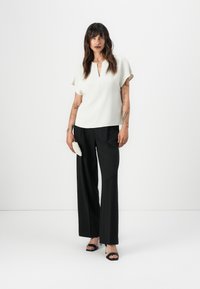 Lichte crèmekleurige blouse met een keyhole-halslijn, korte mouwen; gecombineerd met hoge zwarte wijde broekspijpen en zwarte sleehakken.