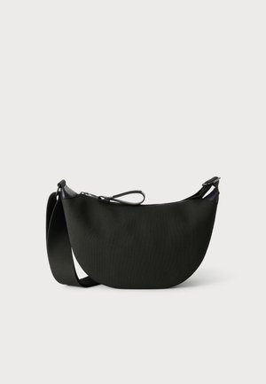 Sac à bandoulière noir en forme de croissant, avec un corps en tissu texturé, une large bandoulière réglable et une fermeture éclair sur le dessus, sur un fond clair et uni.