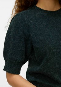 Pull en tricot vert foncé avec des manches courtes et bouffantes. Tissu doux et texturé avec un col rond et un léger éclat.
