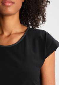 Schwarzes Top mit kurzen Ärmeln und Rundhalsausschnitt, aus glattem Stoff gefertigt. Verfügt über einen kontrastierenden dunklen Saum entlang des Kragens und der Ärmel.