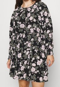 Schwarzes Kleid mit floralem Muster aus pinken und weißen Blumen sowie grünen Blättern. Lange Ärmel, geraffte Taille und lockere Passform.