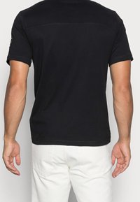 Černé triko s krátkým rukávem vyrobené z hladkého materiálu, s klasickým výstřihem a jednoduchým designem s jediným akcentem na rukávu.