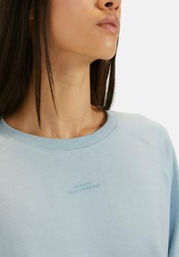 Jasnoniebieska bluza z ribbowanym okrągłym dekoltem, raglanowymi rękawami i wytłoczonym napisem "STWORZONE DO CODZIENNYCH PRZYGÓD".