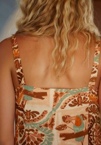 Robe à motifs floraux avec un décolleté carré, larges bretelles, présentant des tons terreux de marron et de turquoise sur un fond crème clair.