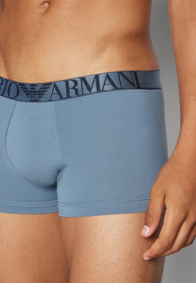 Férfi boxeralsó puha kék textilből, sötétkék gumipánttal, amelyen az "Emporio Armani" logó jól láthatóan szerepel.