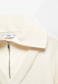 Pull en maille côtelée de couleur crème avec une fermeture éclair à l'avant et un large col, affichant une petite étiquette de marque "MNG" visible.