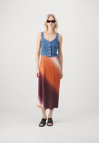 Denim crop top dengan kancing, dipasangkan dengan rok panjang gradasi dari oranye hingga burgundy. Sandal hitam dengan ujung terbuka menyempurnakan penampilan.