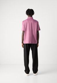 Gaiši rozā kokvilnas polo krekls ar īsām piedurknēm, klasisku apkakli un taisnu apakšmalu, savienots ar brīvi pieguļošām melnām biksēm un baltām kurpēm.