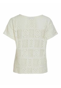 Haut en dentelle blanche présentant un motif géométrique texturé, manches courtes et encolure ronde. Le tissu est léger et semi-transparent.