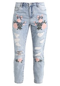 Světle modré seprané džíny s roztrhanými detaily a růžovou květinovou výšivkou na přední straně, vyrobené z denimové tkaniny s uvolněným střihem.
