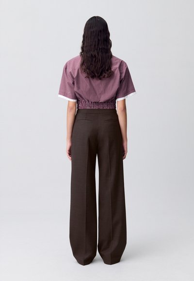 Camicetta corta a scacchi rossi e bianchi con vita elastica, abbinata a pantaloni larghi marroni a vita alta. Tessuti morbidi e design minimalista.