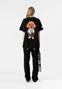 Camiseta negra de gran tamaño con un gráfico de perro de dibujos animados colorido en la parte de atrás, combinada con pantalones negros de corte holgado y una bolsa con detalles impresos.