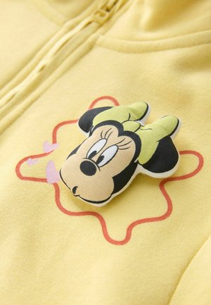 Gelsvas audinys su 3D Minnie Mouse veidu, dėvinčia žalią kaspinėlį, ir raudonu abstrakčios žvaigždės formos kontūru su rožiniais širdelėmis.