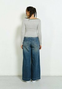 Gray long-sleeve top with a wide neckline, paired with high-waisted, wide-leg blue denim jeans featuring front and back pockets.