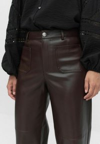 Pantalons en cuir marron avec une texture lisse, dotés de deux poches avant, d'une fermeture à bouton et d'une taille haute.