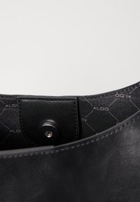 Black synthetic handbag interior with a snap closure and a patterned lining featuring hexagons and "ALDO" text in a subtle design.