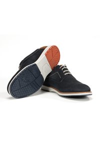 Chaussures en daim navy avec des lacets beige, semelles en caoutchouc léger et accents texturés bleu et orange sur la semelle extérieure. Bout arrondi et design minimaliste.