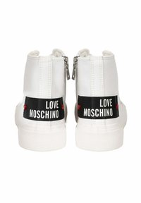 Białe sneakersy typu high-top z tekstylną cholewką, zamkiem błyskawicznym i czarnymi metkami "LOVE MOSCHINO" z tyłu, z czerwonymi akcentami.