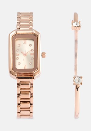 Roze gouden polshorloge met rechthoekige wijzerplaat, Romeinse cijfers en kristalaccenten. Vergezeld van een dunne armband met een enkele kristal.