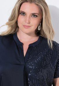 Blusa navy con un tessuto liscio da un lato e una texture decorata con paillettes dall'altro, caratterizzata da un colletto semplice e maniche corte.
