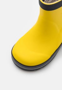 Botte de pluie en caoutchouc jaune vif avec semelle noire et détail de col, sur fond blanc.