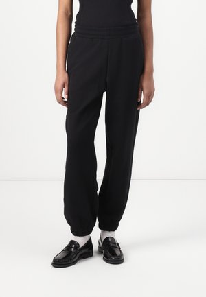 Black, tapered sweatpants with elastic waistband and cuffed ankles, made from soft fabric. Paired with black loafers and white socks.