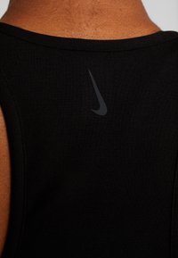 Débardeur de sport noir avec une texture côtelée, arborant un petit logo Nike noir dans le haut du dos. Design simple, sans accents supplémentaires.