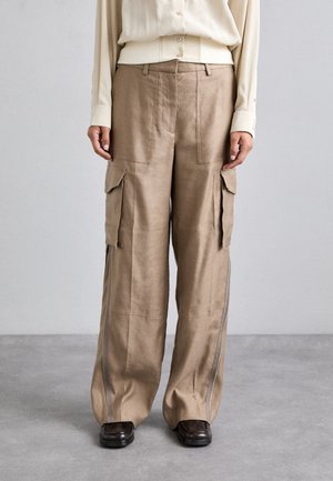 Beige cargo pants with a loose fit, featuring multiple pockets, side zippers, and a smooth texture. Paired with a cream blouse.