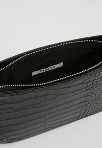 Svart fodral i konstläder med krokodilstruktur, dragkedjestängning och silverfärgad hårdvara. Invändigt klätt med svart tyg och en märkesetikett.