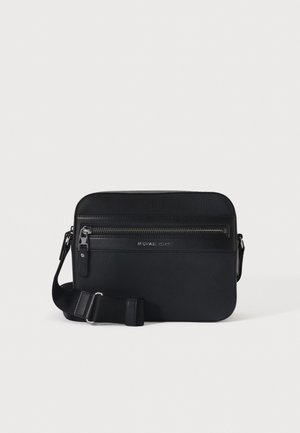Μαύρη ορθογώνια τσάντα crossbody με εμπρόσθια τσέπη με φερμουάρ και ρυθμιζόμενο λουράκι, με το λογότυπο Michael Kors ανάγλυφο κάτω από το φερμουάρ.