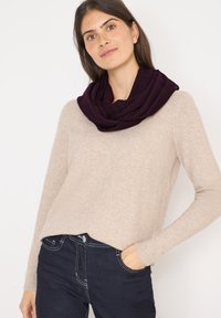 Écharpe infinie violette foncée avec un motif texturé, portée sur un pull beige clair, associée à un jean sombre. Tissu doux avec une apparence confortable.