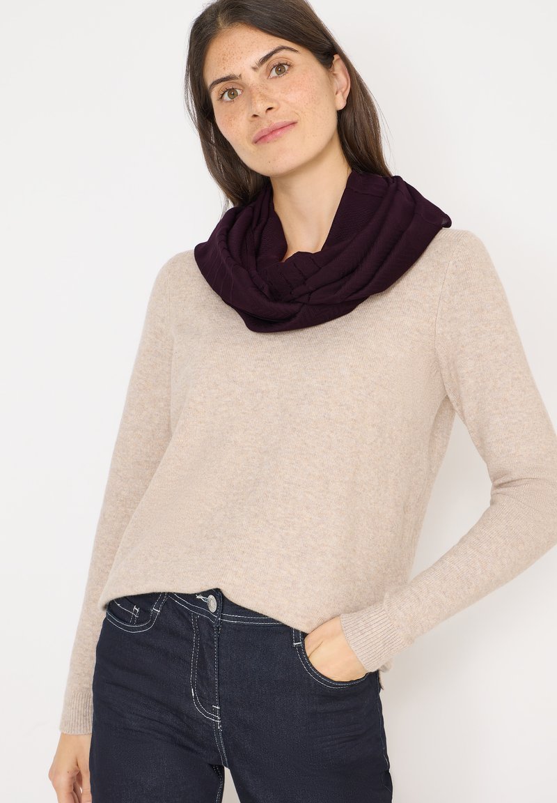 Écharpe infinie violette foncée avec un motif texturé, portée sur un pull beige clair, associée à un jean sombre. Tissu doux avec une apparence confortable.