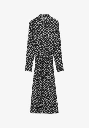 Abito stampato in bianco e nero con colletto, maniche lunghe, apertura frontale con bottoni e una cintura annodata in vita. Silhouette lunga e fluida.