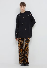 Maglione nero a maglia con dettagli in occhio di pernice argentati, abbinato a pantaloni a gamba larga con stampa animale arancione e nera. Scarpe chunky nere.