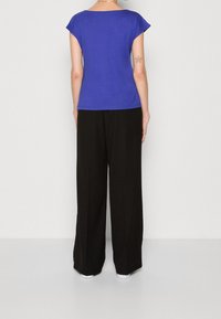 Blue short-sleeve top with a relaxed fit, paired with black wide-leg pants. Smooth fabric, minimal details, and a casual silhouette.
