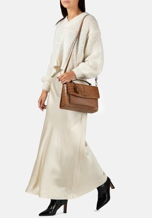 Beige gebreide trui, lange satijnen crèmekleurige rok, zwarte haklaarzen, bruine textuur handtas met een bovenhandvat en schouderband.