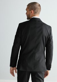 Schwarze maßgeschneiderte Anzugjacke mit glatter Textur, klassischer Passform, mitreissenden Revers und Knöpfen an den Ärmeln, von hinten betrachtet.