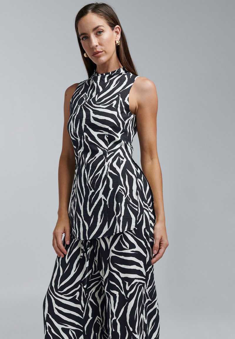 Varrukateta must-valge sebramustriline top, millel on kõrge kaelus ja voogav disain, valmistatud kergest kangast.