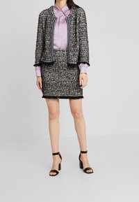 Svart och vit strukturerad tweedjacka med fransade kanter, i kombination med en ljuslila blus och en matchande kjol. Svarta klacksandaler.