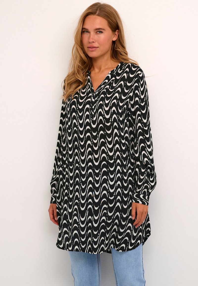Tunique à manches longues noire et blanche à motif ondulé avec un col en V, en tissu lisse, associée à un jean bleu clair.