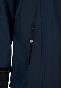 Chaqueta impermeable azul marino con un bolsillo lateral con cremallera, textura suave, puños ajustables y costuras reforzadas.