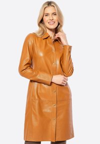 Tan leren jas met een gladde textuur, knoopsluiting aan de voorkant en lange mouwen. Het heeft twee voorzakken en een kraag. Ontworpen met een rechte silhouet.