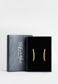 Guldtonade flätade hoopörhängen presenterade i en svart satinerad låda med en texturerad grå utsida och logotyp framtill.