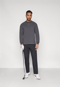 Μακρυμάνικο φούτερ σκούρου γκρι με στρογγυλό λαιμό, συνδυασμένο με μαύρο παντελόνι και λευκά αθλητικά παπούτσια, κρατώντας μία ράβδο γκολφ.