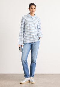 Gestreepte langarm polo in lichtblauw en wit, gecombineerd met lichtblauwe denim jeans en zilveren sneakers. Opvallende knoopsluiting en een relaxte pasvorm.