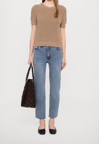 Beige stickad kortärmad tröja, ljusblå raka jeans, svarta balettskor och en mörk vävd tote-väska.