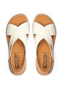 Sandalias deslizantes de cuero blanco con tiras cruzadas y plantilla en tono marrón. Presentan una puntera redondeada y costuras a lo largo de los bordes. Etiqueta de la marca visible.